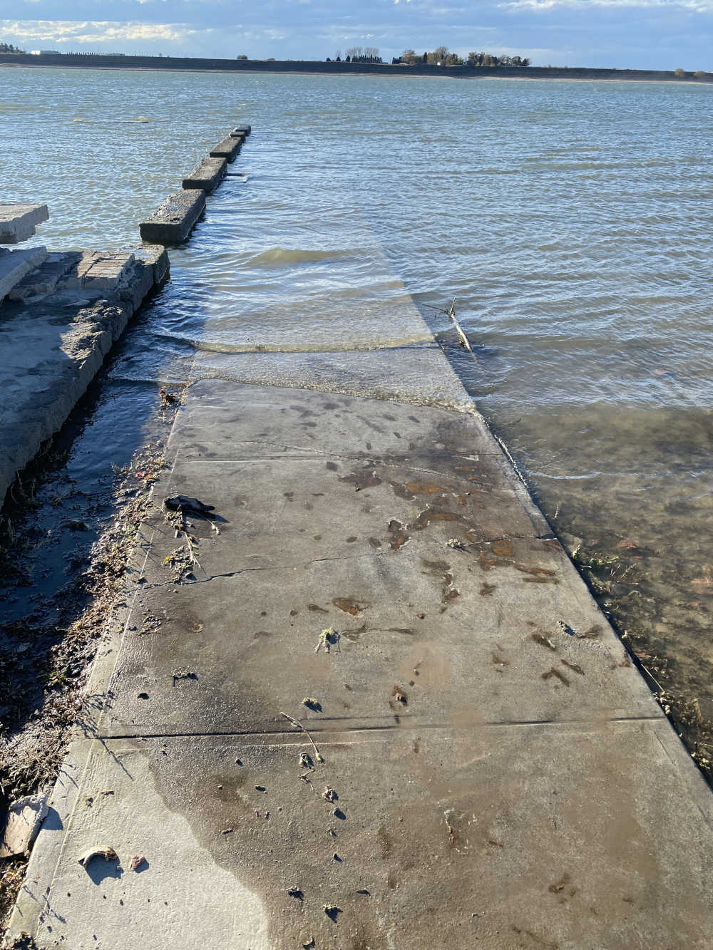 A sidewalk and building foundations disappear into a lake.