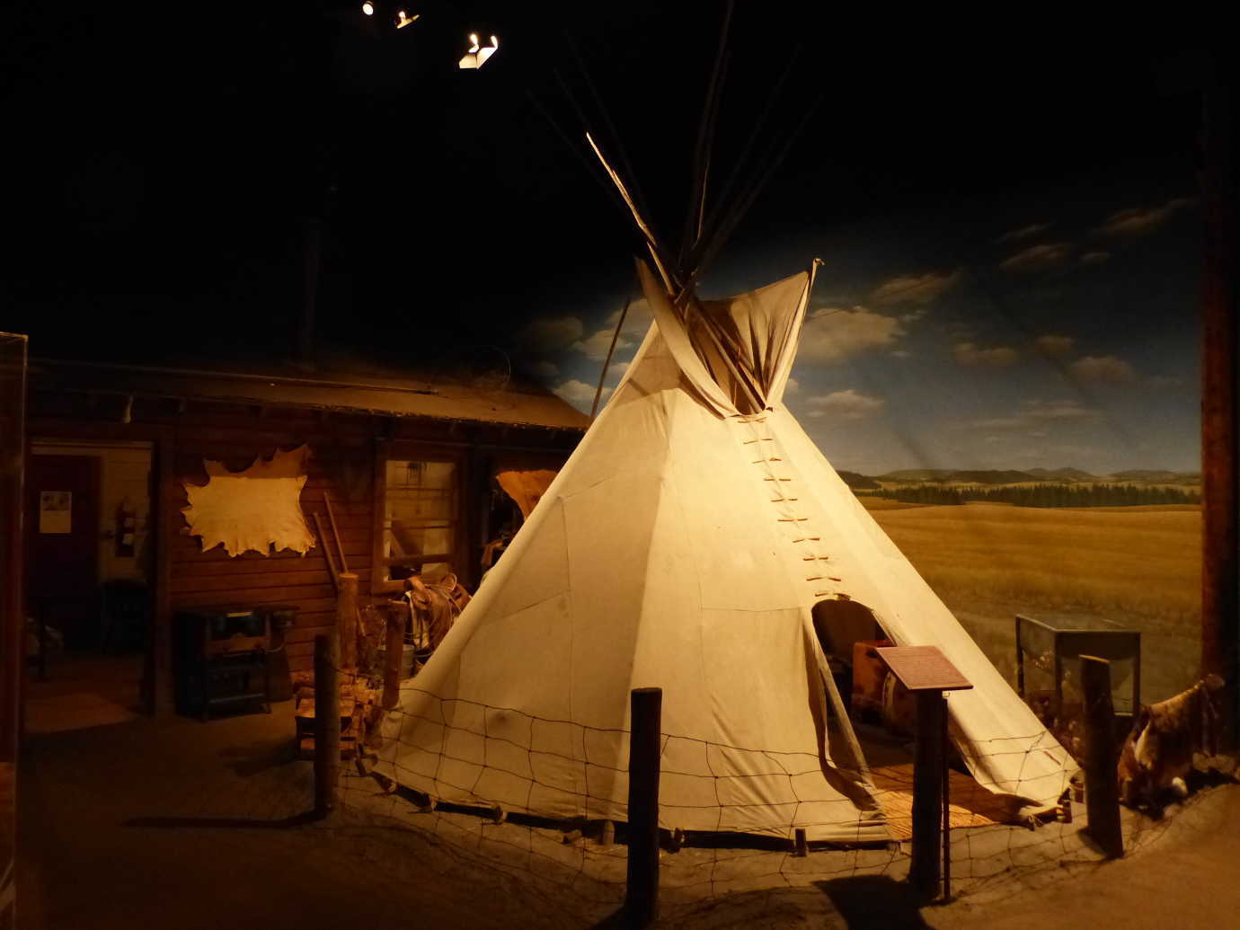 The High Desert Museum&rsquo;s *By Hand Through Memory* exhibition explores the transition of the Plateau American Indians from traditional life to life on the reservations. Here, a traditional tipi is pitched and used outside of a reservation house. The visual pairing of more contemporary times with traditional objects is a striking experience for visitors. Image courtesy of the High Desert Museum.